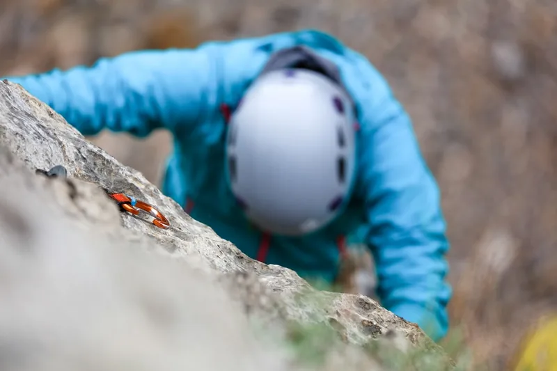 Eine Person trägt einen Kletterhelm während des Kletterns an einer Felswand, Fokus auf Anwendung.