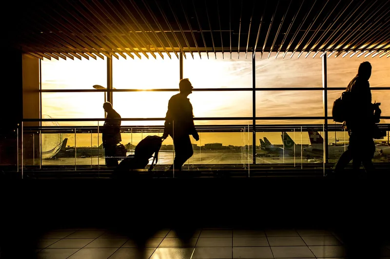 Eine reisende Person zieht einen großen Rollkoffer durch einen belebten Flughafen, dynamische Szene.