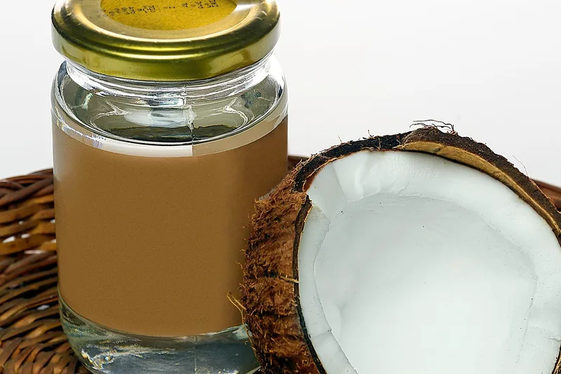 Eine Hand schöpft Kokosöl mit einem Holzlöffel aus dem Glas zur Zubereitung einer gesunden Mahlzeit.