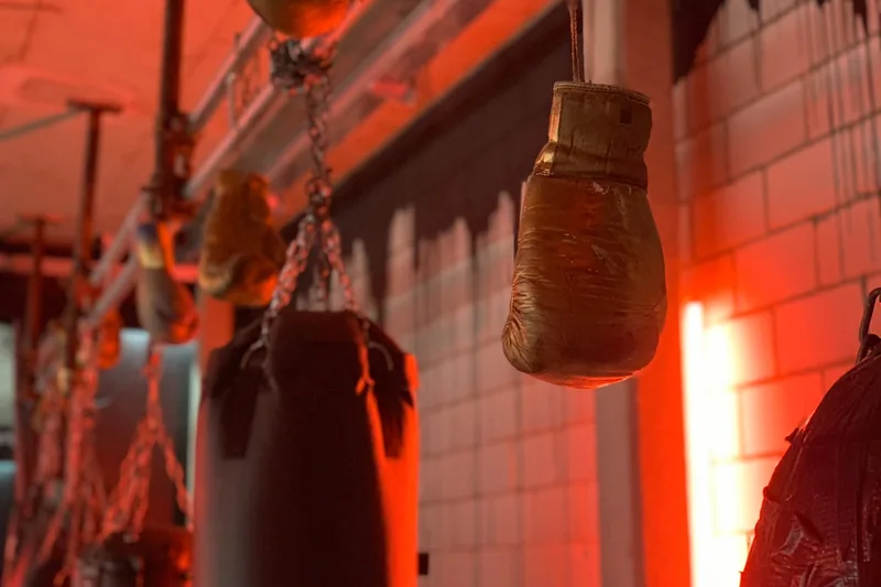Atmosphärische Boxhalle mit Boxsäcken und Trainingsgeräten im Hintergrund, Fokus auf Box-Ausrüstung.