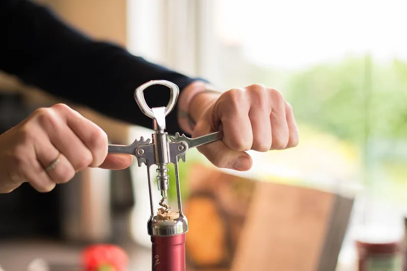 Eine Hand öffnet gekonnt eine Weinflasche mit einem ergonomischen Korkenzieher, Fokus auf die Anwendung.