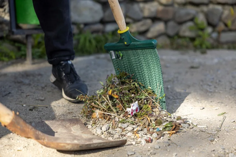 Eine Person kehrt mit einem Krallenbesen effizient Laub von einer Rasenfläche im Garten zusammen.