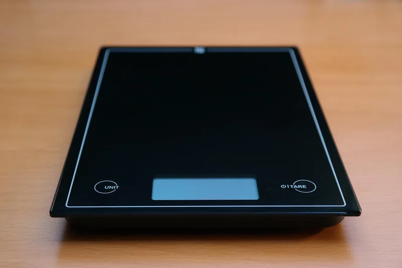 Eine moderne, digitale Küchenwaage aus Glas und Edelstahl, auf einem neutralen Untergrund, sauber und schlicht.