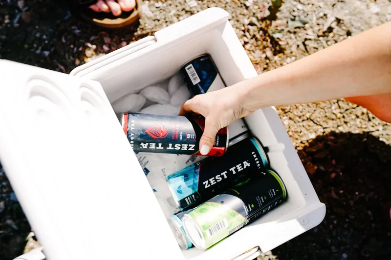 Eine Person öffnet eine Kühlbox am Strand und entnimmt erfrischende Getränke, bereit für den Sommertag.