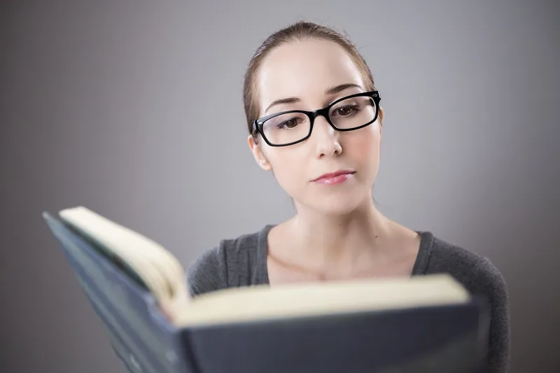 Eine Person liest ein Buch, wobei die Lesebrille klar die Sehhilfe im Einsatz zeigt.
