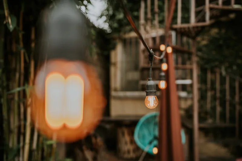 Eine Person befestigt eine Lichterkette an einer Gartenpergola, um den Außenbereich zu beleuchten.