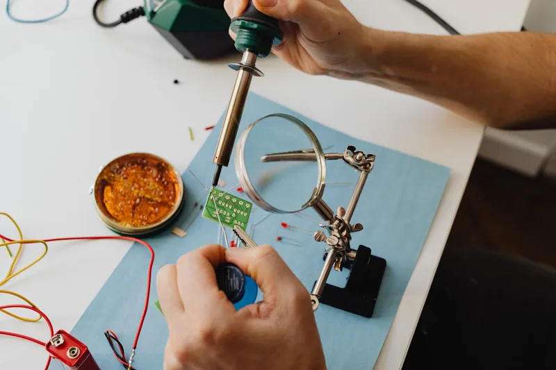 Eine Person lötet präzise elektronische Bauteile auf einer Leiterplatte mit einem Lötkolben, fokussiert auf die Arbeit.