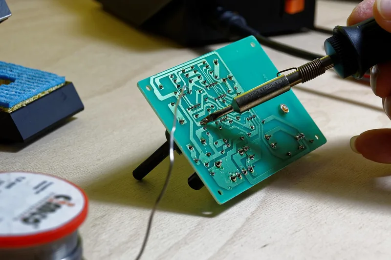 Hände löten eine elektronische Komponente mit einer Lötstation auf einer Platine.