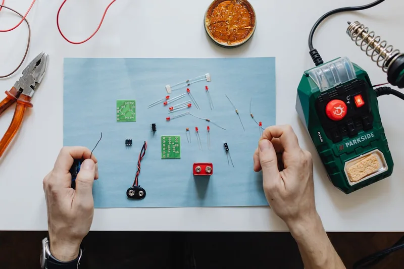 Aufgeräumter Arbeitsplatz mit Elektronikprojekt, Werkzeugen und einer Lötstation im Hintergrund.