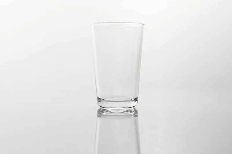 Ein schlankes, leeres Longdrinkglas aus klarem Glas steht auf einer neutralen Oberfläche.
