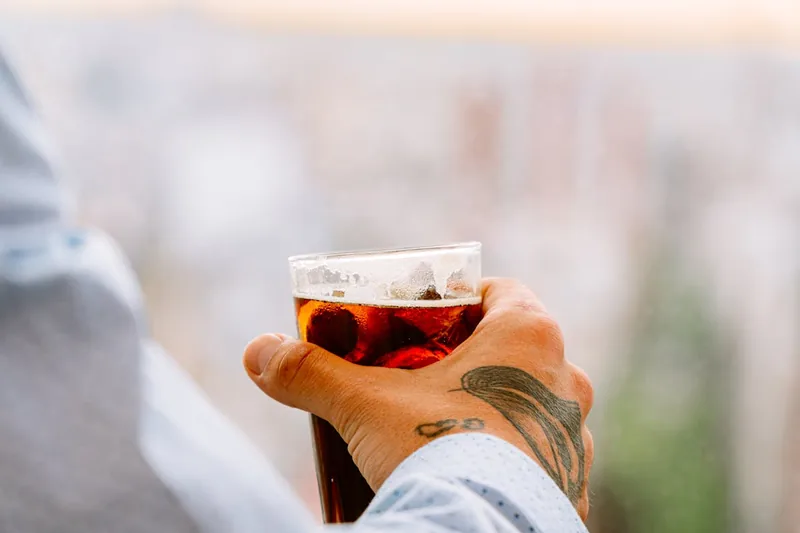 Eine Hand hält ein mit einem erfrischenden Longdrink gefülltes Glas mit Eis und Limettenscheibe.