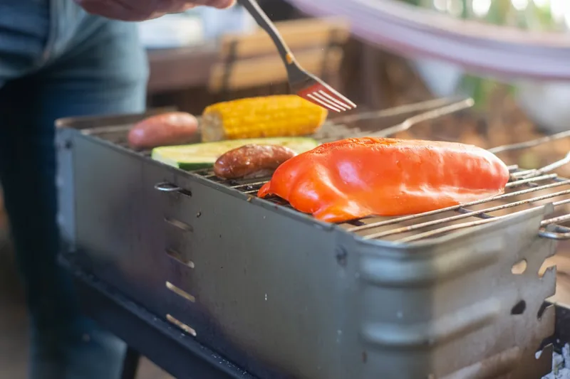 Eine Person grillt frisches Gemüse auf einem Lotusgrill auf dem Balkon, genießt den rauchfreien Komfort.