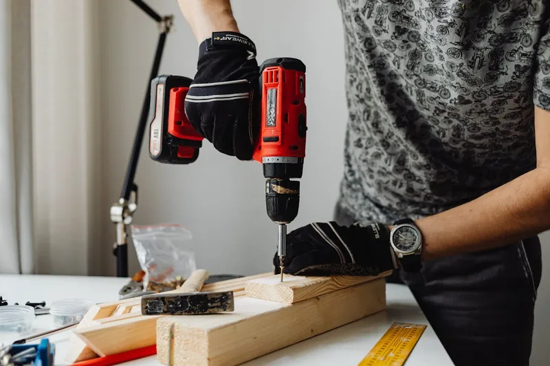 Hand eines Handwerkers verschraubt mit Bit und Akkuschrauber ein Holzbrett, effizientes Arbeiten.