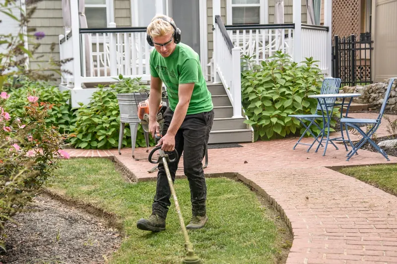 Eine Person trimmt mit einem akkubetriebenen Rasentrimmer Rasenkanten für einen gepflegten Garten.