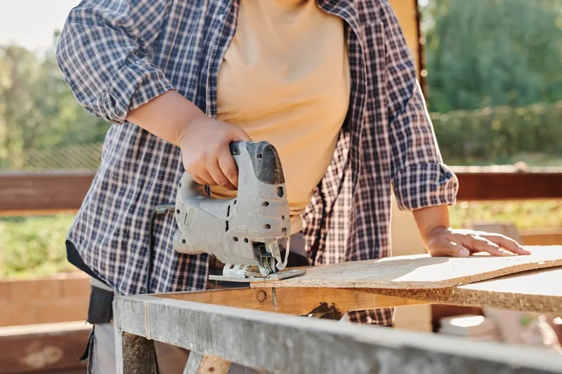 Eine Person sägt mit einer Stichsäge präzise ein Holzbrett, Fokus auf sichere Handhabung des Elektrowerkzeugs.