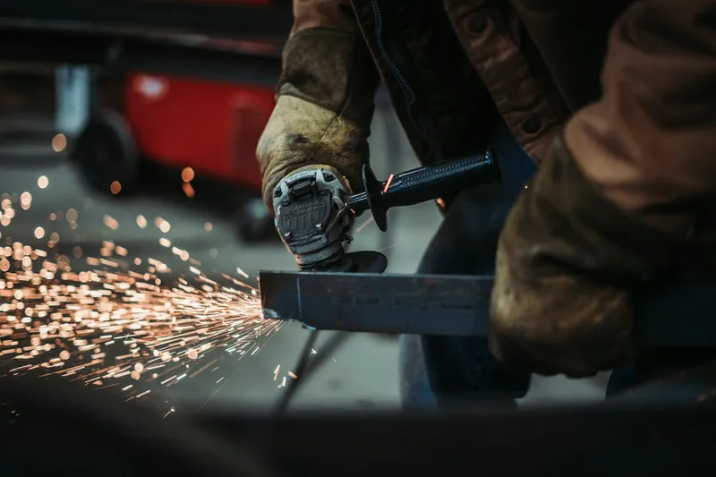 Eine Person benutzt einen Akku-Winkelschleifer, um Metall mit Funkenflug zu trennen, konzentrierte Arbeit.