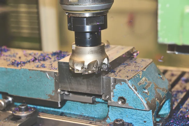 Hand eines Facharbeiters, der ein Metallwerkstück in einem Maschinenschraubstock sicher befestigt.
