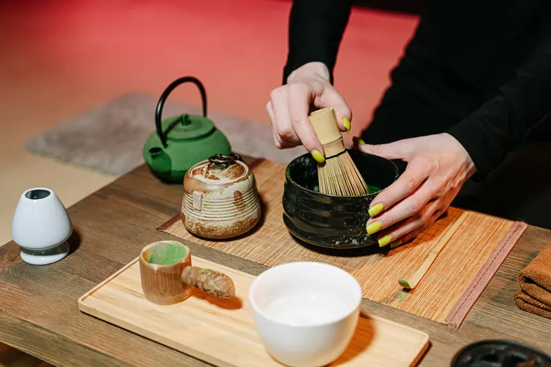 Eine Person bereitet traditionellen Matcha-Tee zu, indem sie mit einem Bambusbesen das Teepulver im Chawan schaumig schlägt.