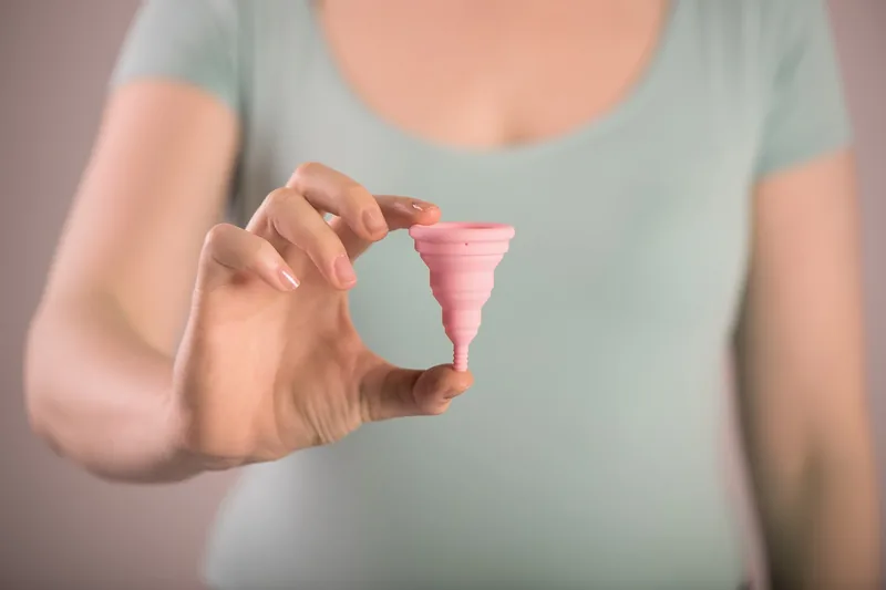 Eine Hand demonstriert das Falten einer Menstruationstasse für die einfache Anwendung während der Periode.
