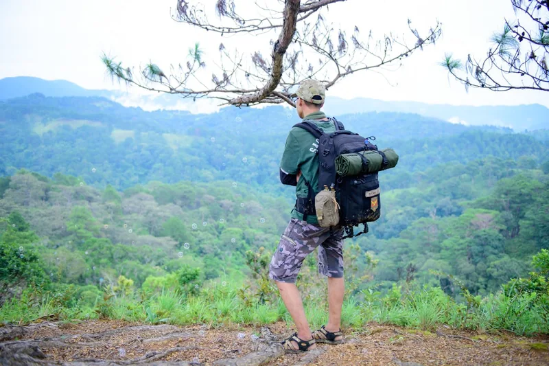 Eine Person trägt einen vollgepackten Militär-Rucksack beim Wandern in bergiger Natur, von hinten gesehen.