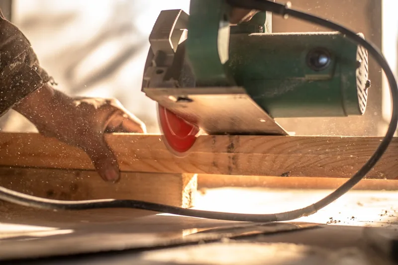 Eine Person schneidet präzise ein Holzbrett mit einer Mini-Handkreissäge, Funkenflug minimal.