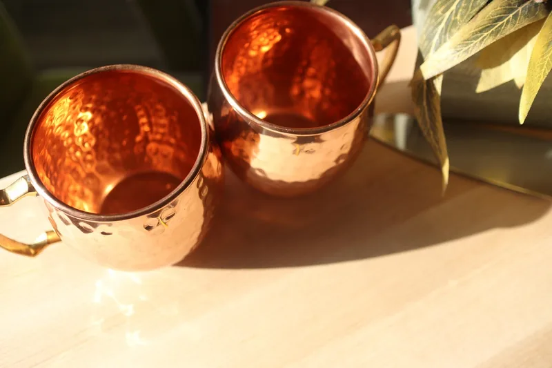 Ein glänzender, leerer Kupfer-Moscow-Mule-Becher im Vordergrund, bereit für den Cocktail.