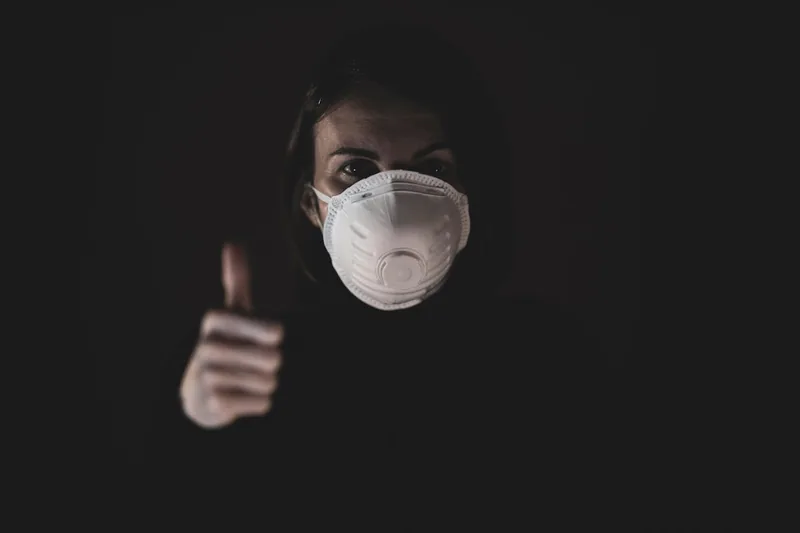 Eine Person trägt eine weiße FFP2 Mundschutz Maske in einer alltäglichen Umgebung, von der Seite aufgenommen.