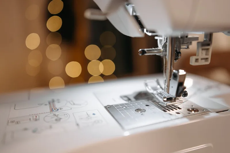 Nahaufnahme des Nähmaschinennadelbereichs, mit Fadenführung und Stichplatte, die präzise Mechanik zeigend.