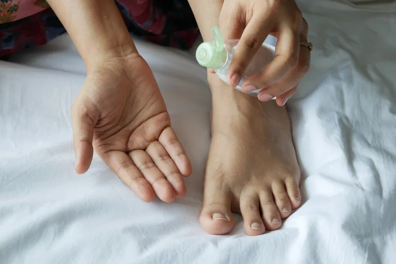 Eine Person trägt ein Nagelpilz-Behandlungsmittel sorgfältig auf die Zehennägel auf, Fokus auf Hände und Füße.