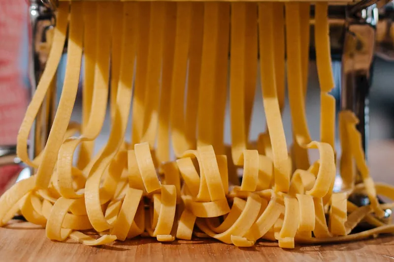 Nahaufnahme des Schneidwerks einer Nudelmaschine, das präzise dünne Pasta-Stränge formt.