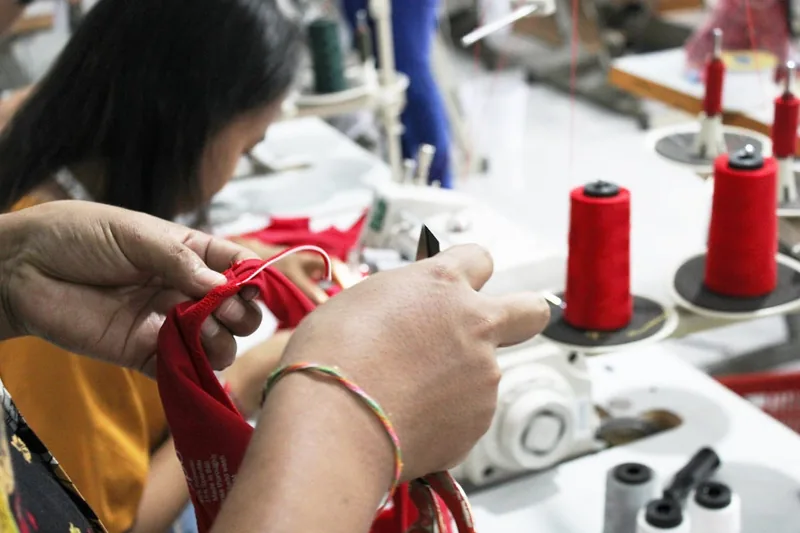 Eine Person näht mit einer Overlock-Nähmaschine am Stoff, die Hände führen das Material präzise.
