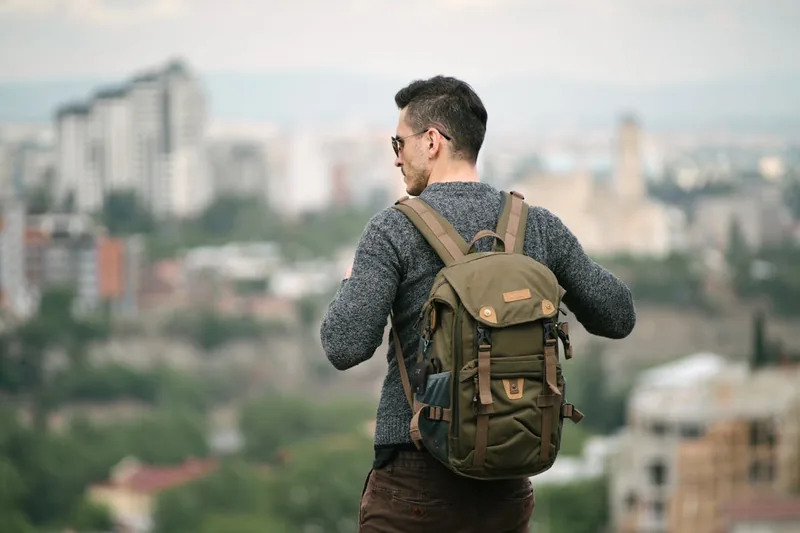 Ein Reisender genießt die Aussicht auf eine Stadt, der diebstahlsichere Rucksack steht sicher daneben.