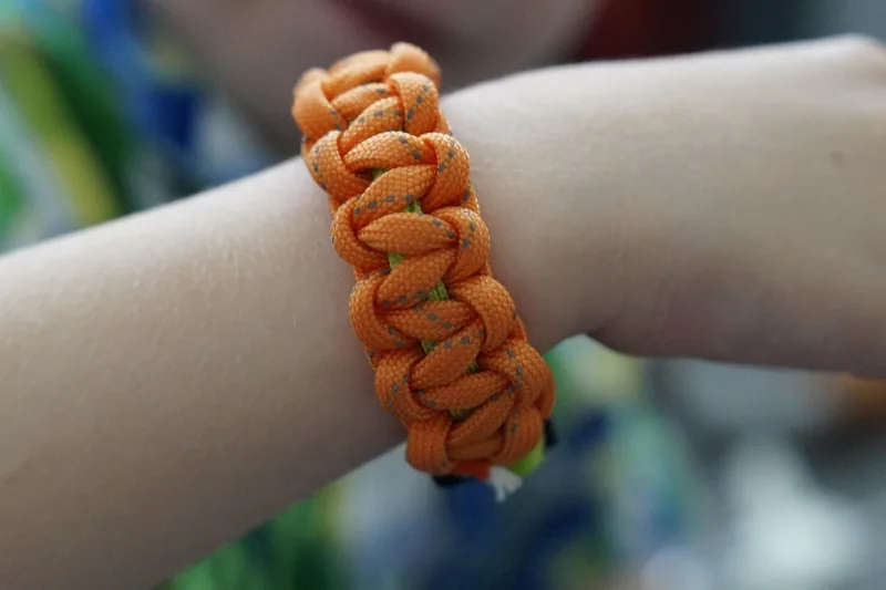 Ein Paracord-Armband am Handgelenk in einer natürlichen Outdoor-Umgebung, symbolisiert Abenteuer.