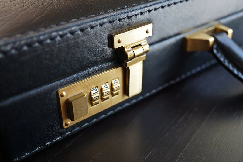 Nahaufnahme eines modernen TSA-Zahlenschlosses und der Oberfläche eines schwarzen Pilotenkoffers aus Aluminium.