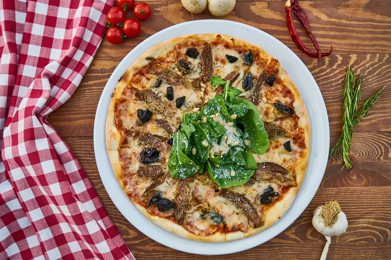 Eine perfekt gebackene Pizza auf dem Holztisch im Garten, umgeben von sommerlicher Atmosphäre und zufriedenen Gästen.