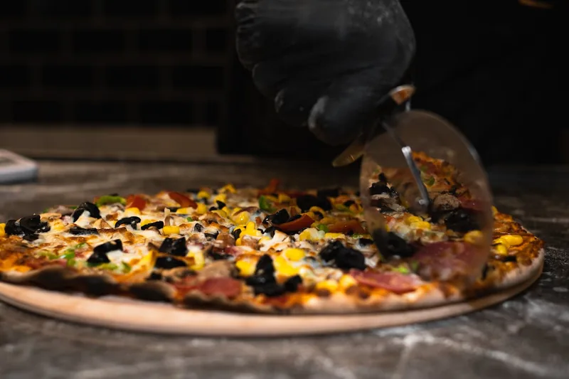Eine Person schneidet eine frisch gebackene Pizza auf einer Küchenarbeitsplatte mit einem Pizzaschneider.
