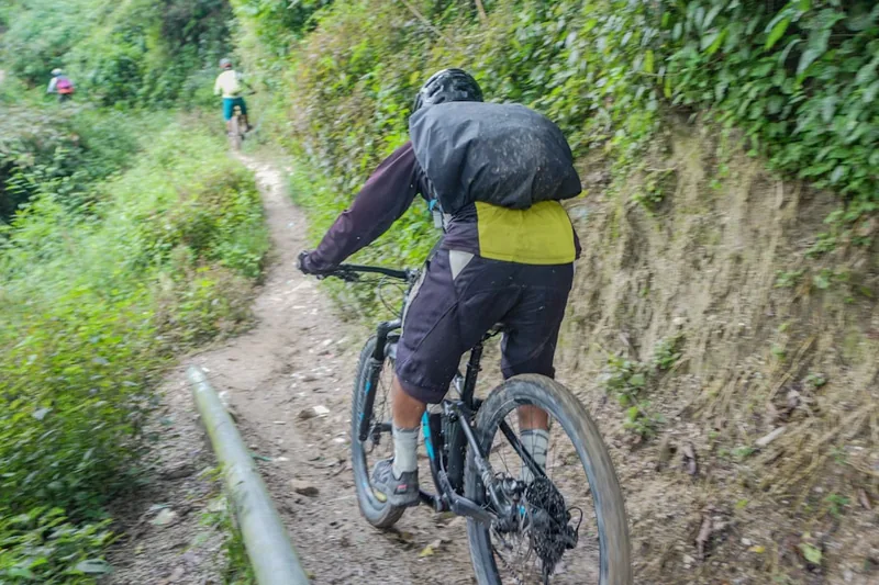 Ein Mountainbiker fährt mit einem Protektor-Rucksack auf einem Trail, Helm tragend und sicher.