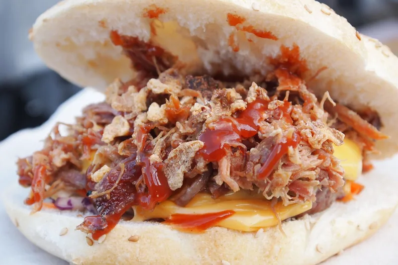 Fertiges Pulled Pork Sandwich auf einem rustikalen Teller bei einem gemütlichen Outdoor-BBQ.