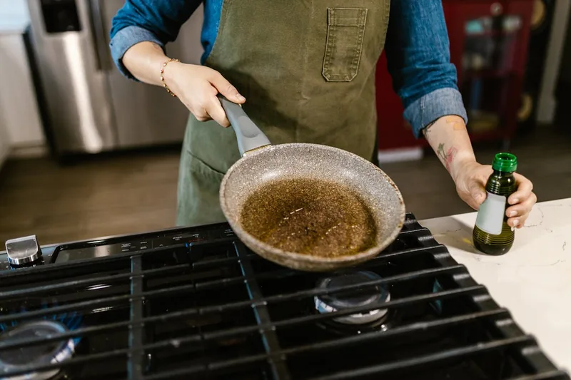 Hände gießen Rapsöl in eine Pfanne beim Kochen.