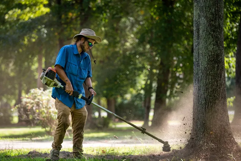 Eine Person trimmt präzise Rasenkanten mit einem Akku-Rasentrimmer im gepflegten Garten.