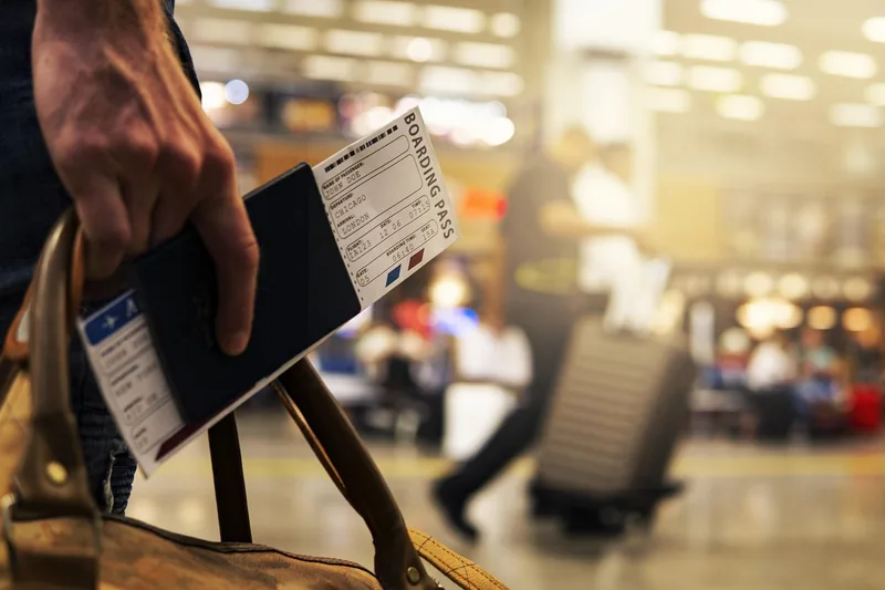 Eine Person zieht mühelos eine Reisetasche mit Rollen durch einen belebten Flughafenbereich vor dem Abflug.