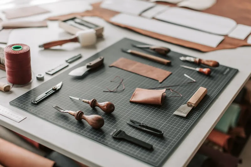 Ein Kreativ-Workshop-Tisch mit Lederstücken, fertigen Accessoires und einer Lochzange, symbolisiert Bastelideen.