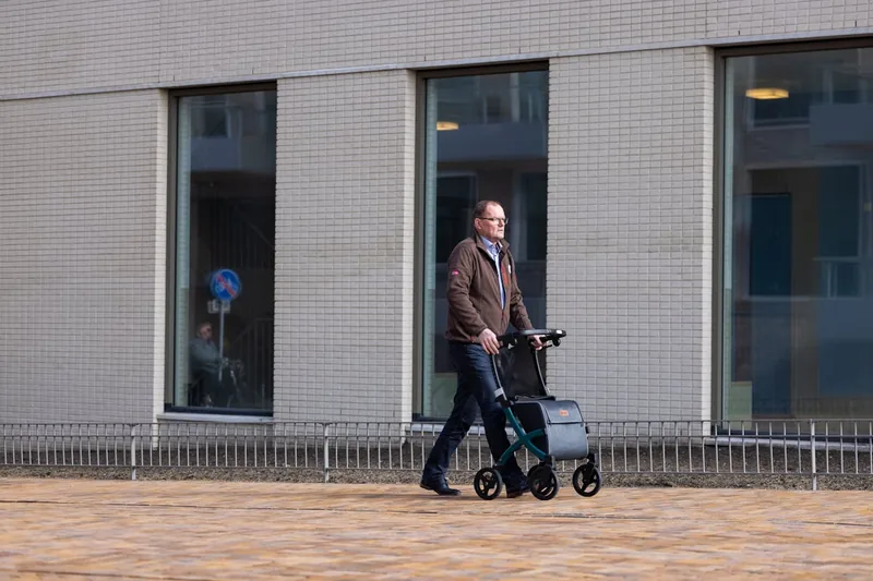 Person (Senior) nutzt einen Rollator mit Einkaufstasche für mehr Mobilität und Komfort beim Spaziergang.