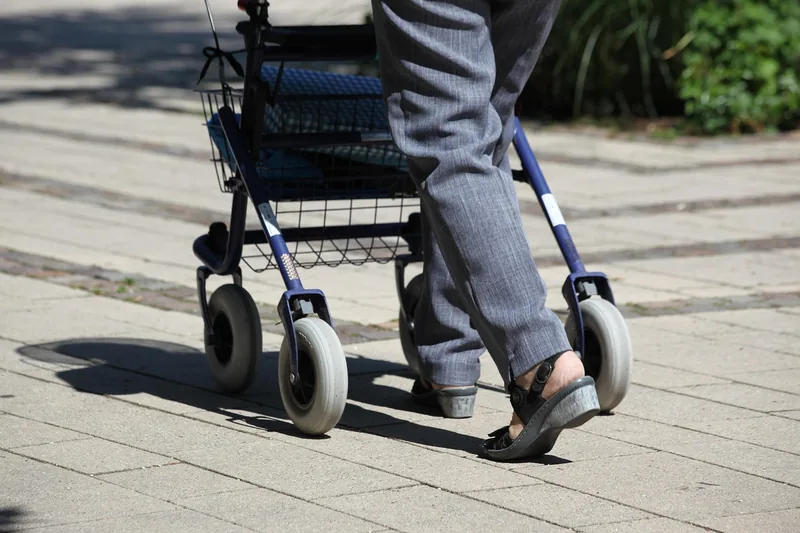 Ein Rollator steht gefaltet neben einer Parkbank und symbolisiert selbstbestimmte Mobilität im Alltag.