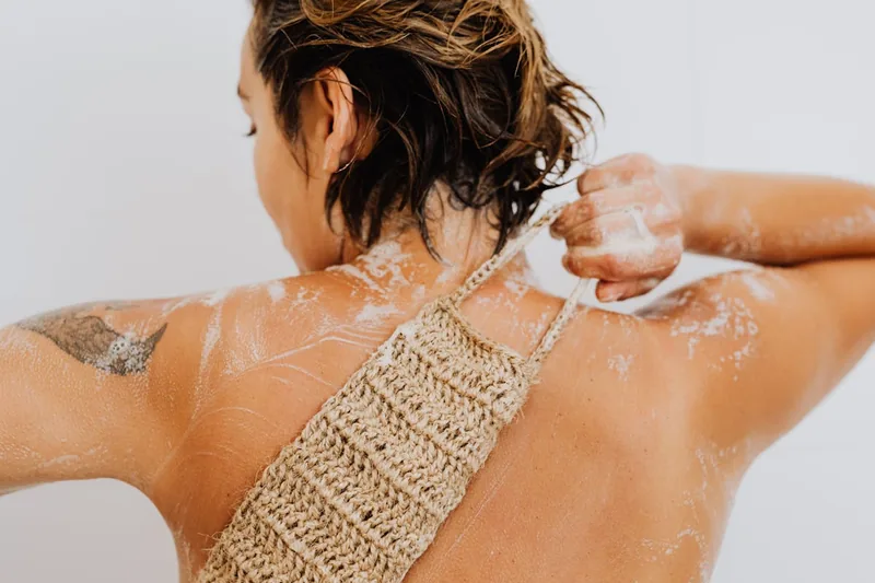 Eine Person benutzt einen Rückenschrubber unter der Dusche zur Reinigung.