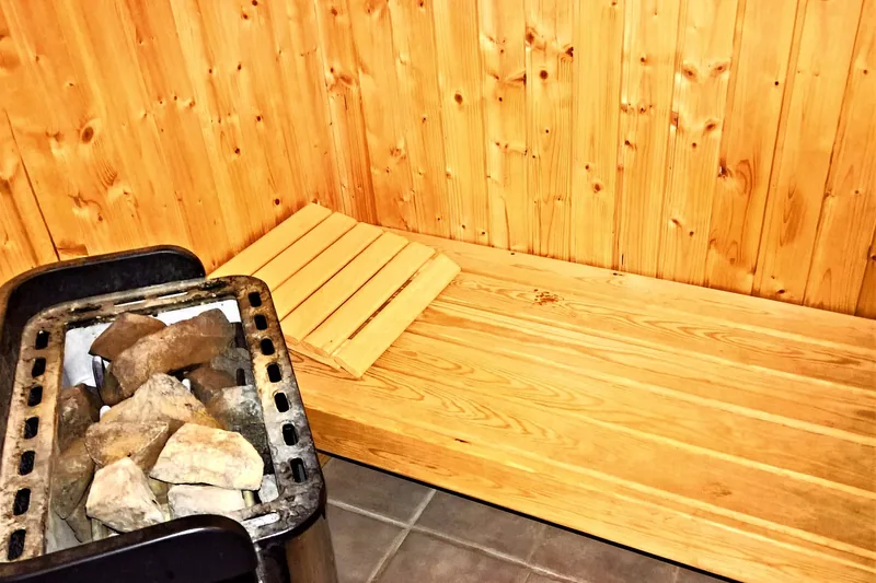 Einladende Sauna-Kabine mit gedämpftem Licht und einem Saunaofen im Hintergrund, die zum Entspannen einlädt.