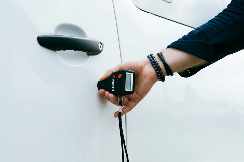 Eine Person misst die Lackdicke eines Autolacks mit einem Schichtdickenmessgerät, um Qualität zu prüfen.