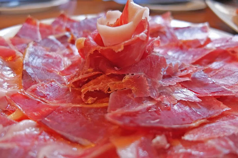 Eine appetitliche Szene mit fertig geschnittenem Schinken und Tapas auf einem Küchentisch angerichtet.
