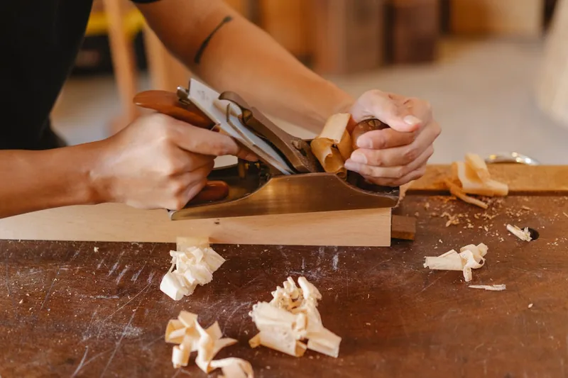 Eine perfekt geglättete Holzoberfläche auf einer Werkbank, umgeben von Holzspänen, als Ergebnis der Arbeit mit einem Schlichthobel.
