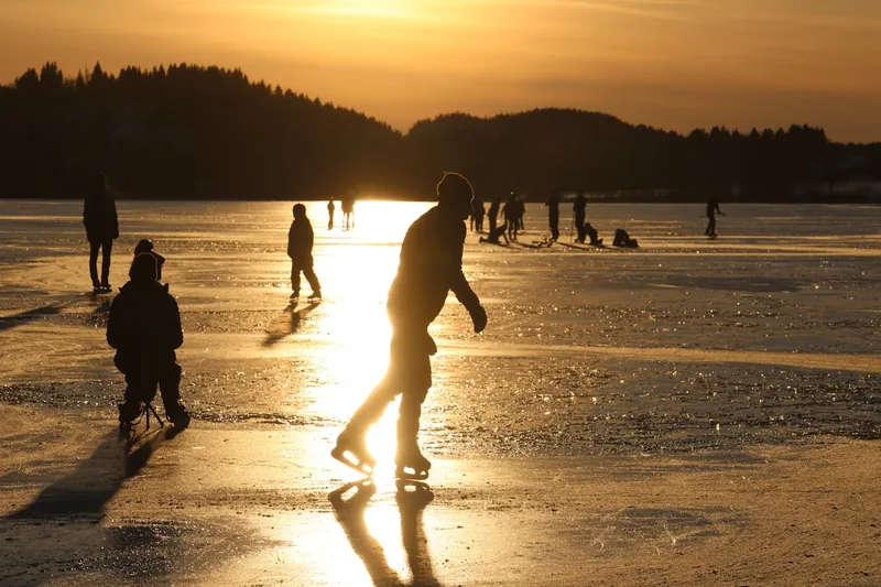 Eine idyllische, winterliche Eislaufbahn im Freien mit Menschen, die das Schlittschuhlaufen genießen.
